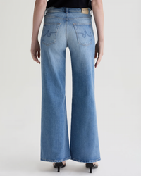 A person wearing AG Jeans' Saige Wide Leg in 18Ys Bisou—a light blue, high-rise, wide-leg cropped jean—paired with black heeled sandals, shown from the back against a plain light background.