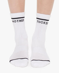 A pair of feet wearing Mother’s MF Baby Steps in White—vintage-inspired tube socks with black stripes and “MOTHER” and “FUCKER” across the top.