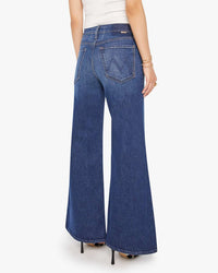 A person is seen from the back wearing Mother’s Lil Tomcat Roller Skimp in Perfectly Imperfect—high waisted, wide leg jeans with large back pockets and flared bottoms—paired with a white top and black high heels.