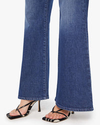 A person wearing the Lil Tomcat Roller Skimp in Perfectly Imperfect jeans by Mother and black strappy high-heeled sandals with white accents, standing against a plain white background.