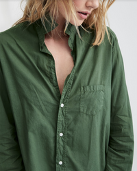 A person with blonde hair wears the Frank & Eileen Eileen Relaxed Button Up Shirt in Army Green, made from 100% cotton with a chest pocket. Shown from shoulders to mid-torso, their face is partially out of frame.