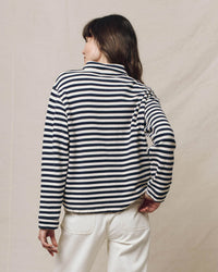 A person is seen from behind wearing the Greats Rugby Sweatshirt in Navy Sailor Stripe paired with white pants, set against a neutral backdrop.