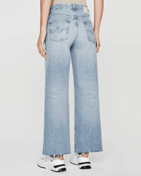 Someone is shown from the back against a plain background, wearing AG Jeans Saige Wide Leg Crop in Chateau with a high-rise waist, frayed hems, and white sneakers.