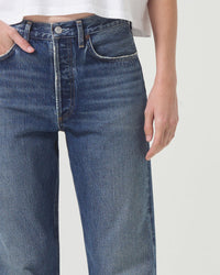 A person wearing AGOLDE’s 90s Jean in Imagine and a white cropped shirt stands against a plain light background, showing only their torso and upper legs. One hand is in a pocket while the other rests at their side.