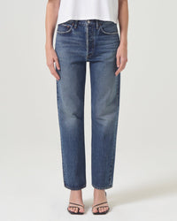 A person stands against a plain white background in AGOLDE’s 90s Jean in Imagine—high-waisted, straight-leg denim—paired with a white sleeveless top and black open-toe sandals.