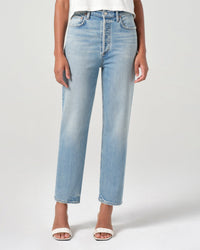 A person wears AGOLDE’s 90s Pinch Waist Crop in Ripple—light blue, high-rise cropped straight leg jeans—with white open-toe heels, standing against a plain light gray background.
