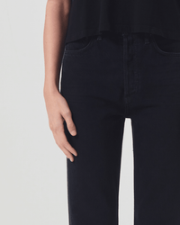 A person in a black top and AGOLDE 90s Pinch Waist in Crushed jeans stands with their left hand relaxed by their side, visible from mid-torso to upper thigh against a plain background.