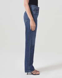 A person in AGOLDE’s 90s Pinch Waist Long in Control jeans, a black top, and black heeled sandals stands sideways against a plain white background.