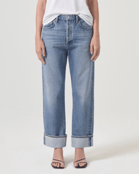 A person wears AGOLDE's Fran Low Slung Straight in Invention jeans with large rolled cuffs, a white tucked-in shirt, and black open-toe heeled sandals, standing against a plain light background.