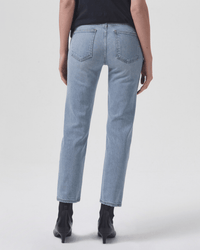 A person stands with their back to the camera against a white background, wearing AGOLDE’s Kye in Diversion jeans—light blue, mid-rise, straight leg—paired with black ankle boots.