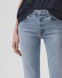A person wears AGOLDE's Kye in Diversion jeans—light blue, vintage-inspired, with a mid-rise straight leg fit—paired with a dark navy t-shirt. The image highlights the waist and upper thighs against a plain background.
