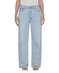 A person stands facing forward in light blue, high-waisted AGOLDE Low Slung Baggy in Fragment jeans and a white top. Their hands are at their sides and they wear open-toed heels, showcasing a modern look from AGOLDE.