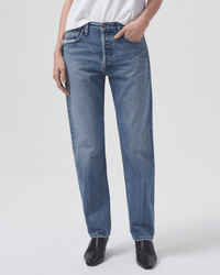 A person is wearing a white t-shirt and AGOLDE Parker Long in Invention straight leg jeans with hands in pockets, standing against a plain light background. Only the body from shoulders down is shown. They are also wearing black shoes.