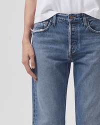 A person wearing a white t-shirt and AGOLDE Parker Long in Invention jeans with frayed detailing on the left pocket, shown from waist to mid-thigh against a plain background.