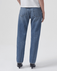 A person is shown from the back against a plain white background, wearing AGOLDE Parker Long in Invention jeans with a white shirt and black heeled shoes.