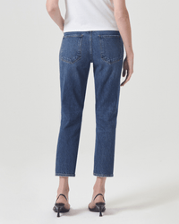 A person in a white top, AGOLDE Riley Crop in Control high-rise straight leg jeans, and black heeled sandals stands facing away with arms relaxed by their sides against a plain light background.