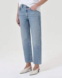 Person wearing AGOLDE Valen Jean in Harmonic, a light blue denim style, paired with a white t-shirt and white pointed-toe shoes. Only the lower half of the body is visible against a plain light background.