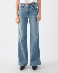 Someone wearing the AMO Anita Flare in Eternal, high-waisted light blue wide-leg jeans with a slight fade, paired with a white crop top and black shoes, stands against a plain light background.