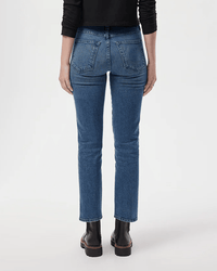 A person stands facing away against a light background, wearing AMO Chloe Crop in True Love jeans paired with a black long-sleeve top and black ankle boots.