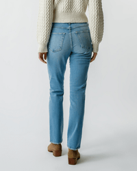 A person is wearing the AMO Chloe Long Length in Liason jeans, paired with a cream textured sweater and tan heeled boots, standing with their back to the camera against a plain white background.