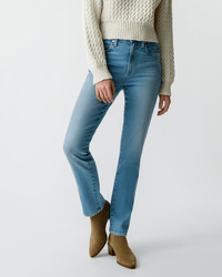 A person wears the AMO Chloe Long Length in Liason jeans, styled with a textured cream sweater and tan ankle boots, standing against a plain white background. Their face is not visible in the image.