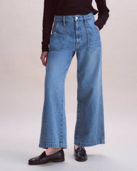 Person wearing the AMO Diana Pant in Outlander, featuring high-waisted, wide-leg style with army patch pockets, paired with a black long-sleeve top and black loafers against a light beige background.