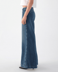 Seen in profile against a plain light background, only the lower body is visible. The person wears a white short-sleeve top paired with the Edith Wide Leg Trouser in Romance by AMO.