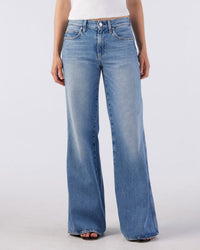A person wearing AMO's Faith Flare in Maverick jeans and a white sleeveless top stands against a plain light background. The image is cropped from the shoulders down.
