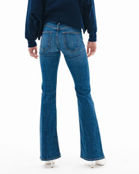A person wearing ASKK NY's Bond Street in Paris jeans stands facing away from the camera against a white background, styled with a dark blue sweater and white heeled shoes.