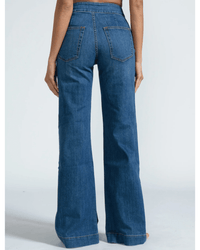 A person stands facing away from the camera wearing ASKK NY's Brighton Wide Leg in Mercury jeans, made from Japanese stretch denim with two back pockets and visible brown stitching, set against a plain light background.