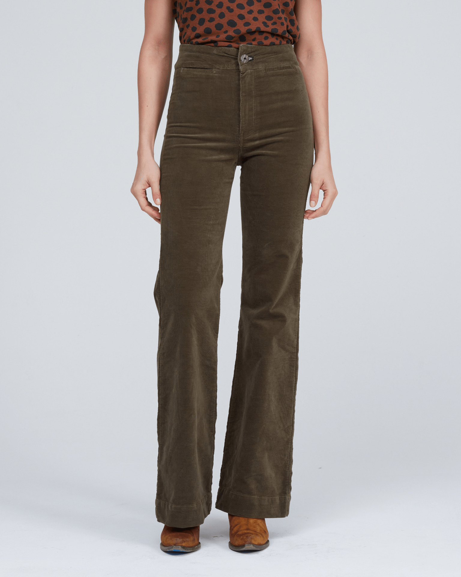 A person wears the ASKK NY Brighton Corduroy Wide Leg in Safari Green, paired with a brown and black spotted top and brown shoes, standing against a plain light background.