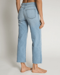 A person stands barefoot, seen from the back, wearing ASKK NY Crop Wide Leg in Zuma jeans with raw, frayed hems and large back pockets against a plain light background.