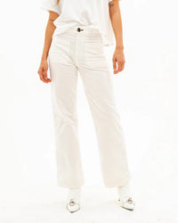 A person, visible from the waist down, stands against a plain white background wearing ASKK NY’s Sailor Corduroy in Eggshell and white shoes with silver buckles.