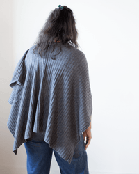 A person with long dark hair, dressed in blue jeans and the Autumn Cashmere Rib Drape Poncho in Flannel, faces away from the camera against a plain white background.