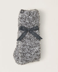 A pair of Barefoot Dreams CC Heathered Socks in Slate Blue/White is neatly folded and tied with a black ribbon featuring the brand name, displayed on a plain light background.