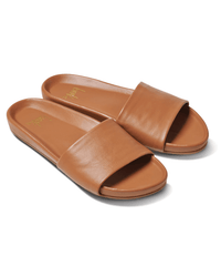 The Gallito in Tan by beek. features brown leather slides with wide single straps and flat, memory foam soles, shown against a white background.