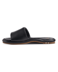 The Puffbird in Black by beek. is a black slide sandal with a wide single strap, flat sole, molded arch support, and minimal detailing, shown in side profile on a white background.