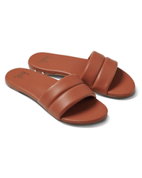 The beek.. Sugarbird in Tan is a pair of brown leather slide sandals with wide, padded straps, open toes, and a molded footbed, shown at an angle on a white background.