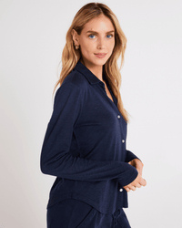 A woman with long blonde hair, dressed in the Bella Dahl Button Up Knit Top in Endless Sea and matching pants, stands sideways and smiles at the camera against a plain light background.