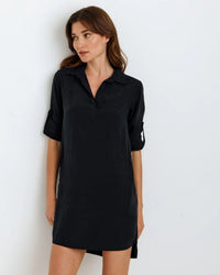 A woman models the Bella Dahl L/S A Line Shirtdress in Vintage Black, a loose-fitting TENCEL Lyocell dress with rolled-up long sleeves, standing against a white background and looking slightly to her left.