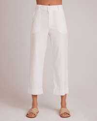 Wearing Bella Dahl’s Saige Wide Leg Crop in White, a person stands against a plain light background in tan slide sandals; only the high rise, wide leg, linen-cotton blend pants are visible. Upper body is not shown.