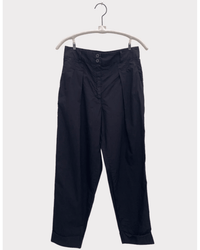 The Inez - Parachute in Black by A Shirt Thing, a pair of high waist black trousers with a pleated front, button closure, and side pockets, is displayed on a white hanger against a plain white background.