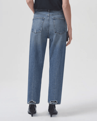 Person wearing AGOLDE 90s Crop Mid Rise Loose Straight in Hooked—mid-rise, loose, straight-leg blue jeans with frayed hems—paired with black heeled boots, shown from the back against a plain light background.