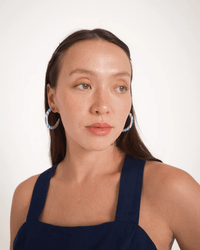 A woman with long brown hair wears B&L’s C Hoop in Small in Places You’ll Go earrings—colorful mango wood pieces handcrafted by Filipino artisans—and a sleeveless navy blue top, looking slightly to the side against a plain white background.