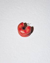 A small, round, reddish-brown electronic component with two metal pins and red square marks rests on a textured white surface, echoing the intricate detail of B&L’s Mini Chunk Hoop in Grace.