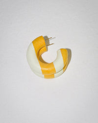 A chunky Small Chunk Hoop in Limone by B&L, featuring alternating matte yellow and white stripes, lies on a textured white surface. The bold circular design and visible metal posts recall sporty 90’s style.