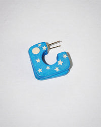 The B&L Square Mini Hoop in Goodnight Moon features blue, square-shaped earrings with white star and moon designs, a metallic post, and is shown on a plain white background.