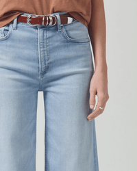 Wearing Citizens of Humanity Lyra Crop Wide Leg in Marquee, styled with a brown belt and rust top, only the lower torso and one arm with a silver ring are visible against a light background.