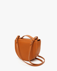 The Clare V. Elodie in Cuoio is a small tan crossbody crafted from Italian vachetta leather with top handles, a rounded bottom, and an adjustable strap, shown against a plain white background.
