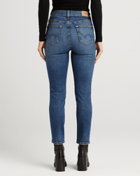 A person is shown from the back against a plain light background wearing a black long-sleeve top, black heeled boots, and Edwin Bree in Abbot ankle length jeans.